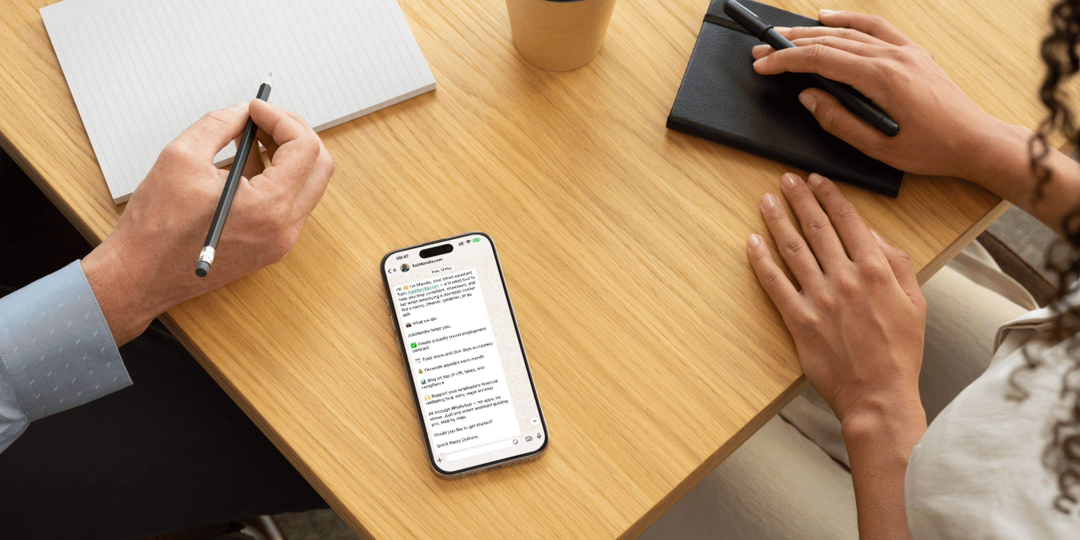Two people sitting at a table with a phone with WhatsApp open on the AskMandla chat